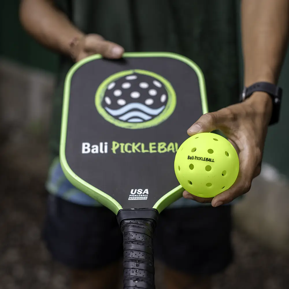 Bali Pickleball staff handing a paddle to a first-time player at our jungle courts in Amed